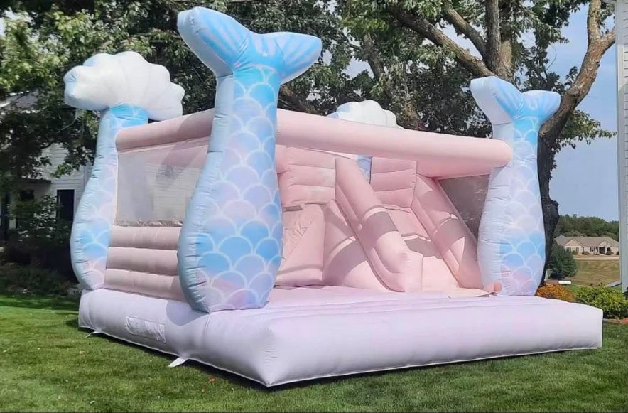 Pastel pink and blue mermaid-themed bounce house with slide on a green lawn